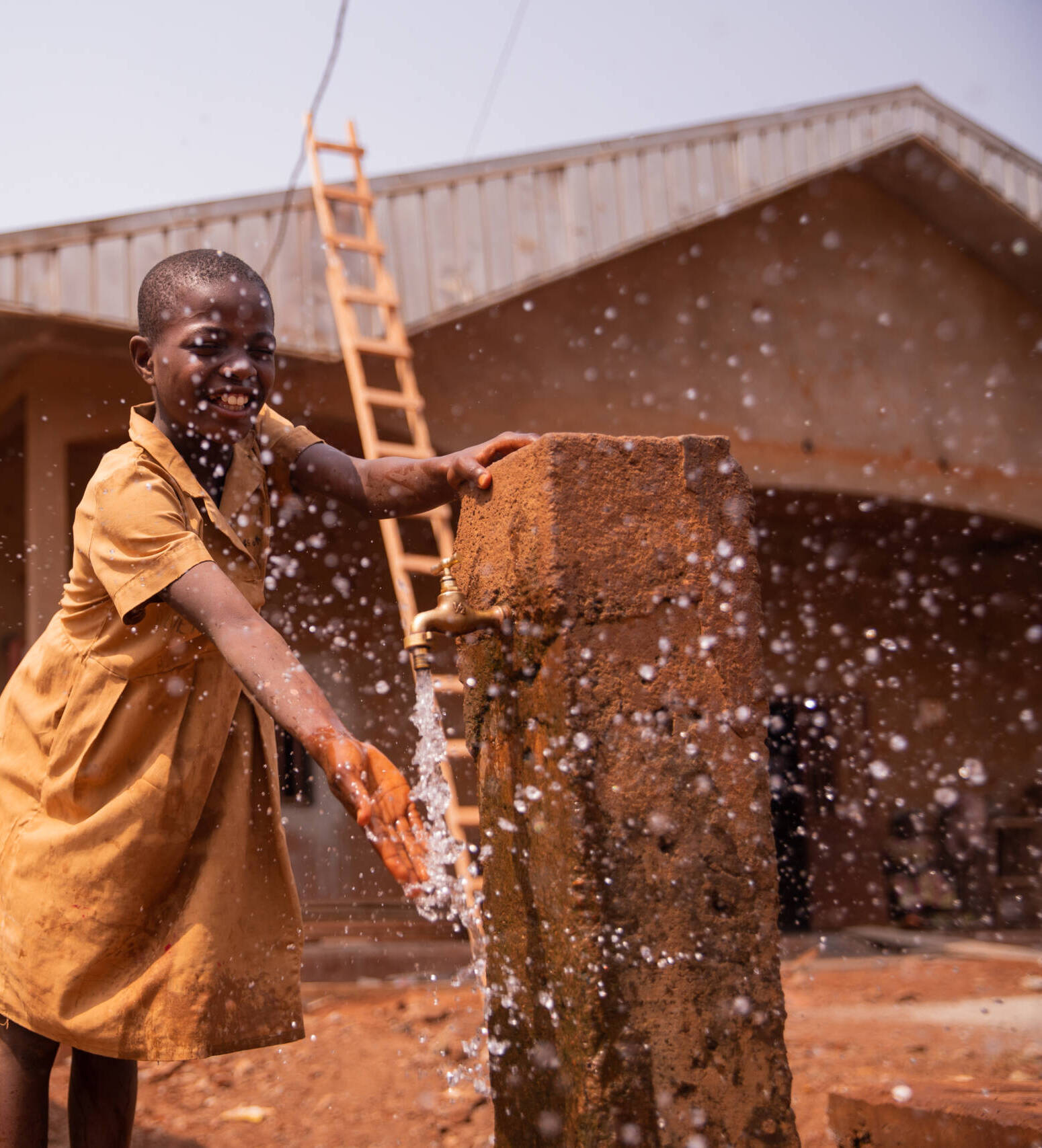African schoolchild plays splashing water from the tap placed outside in the schoolyard.